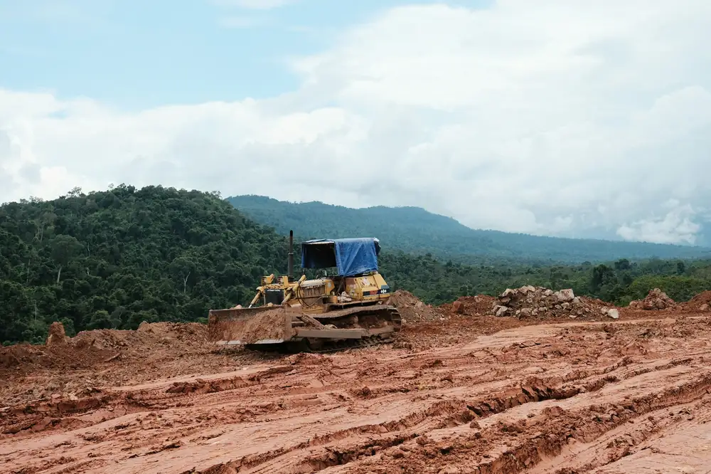 Dozer working red soil on a cleared site below green hills