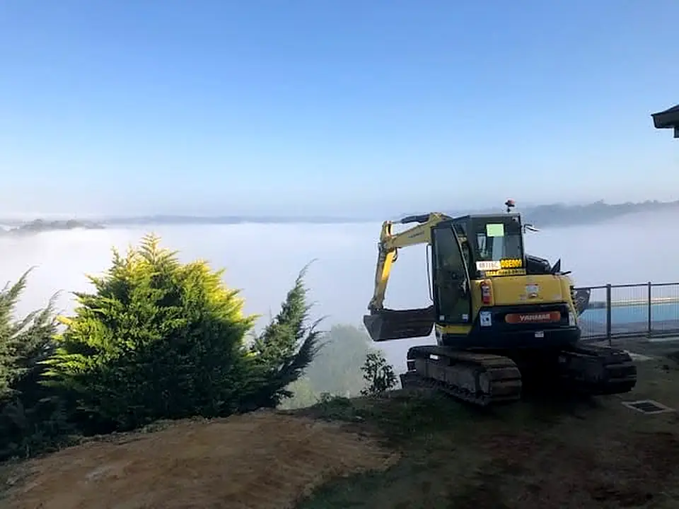 Excavator on a hilltop site above a misty valley