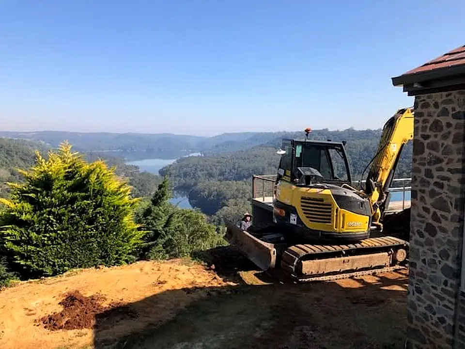Milako excavator working close beside a stone house on a hillside