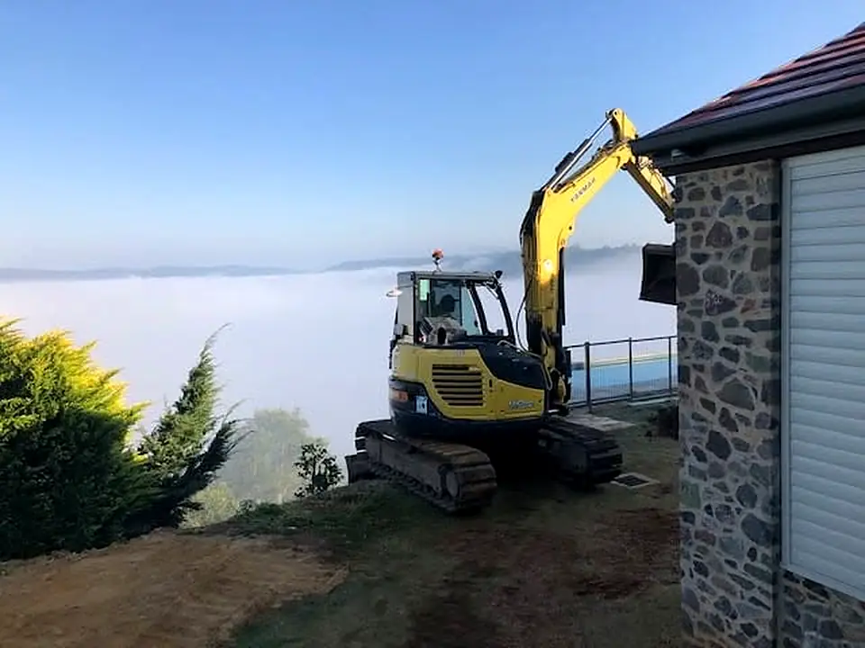 Excavator beside a stone house with fog in the valley below