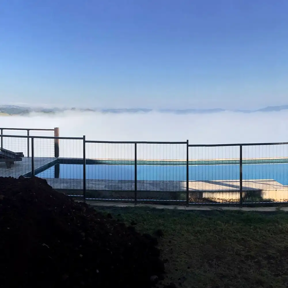 Fenced pool above a valley full of morning fog, with fresh earth in front