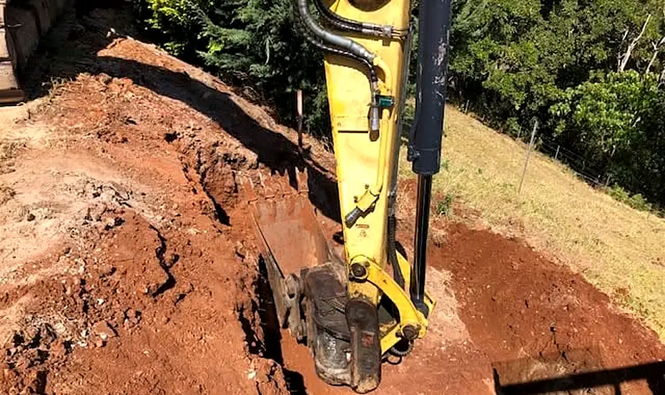 Milako excavator bucket digging a trench in red soil on a slope